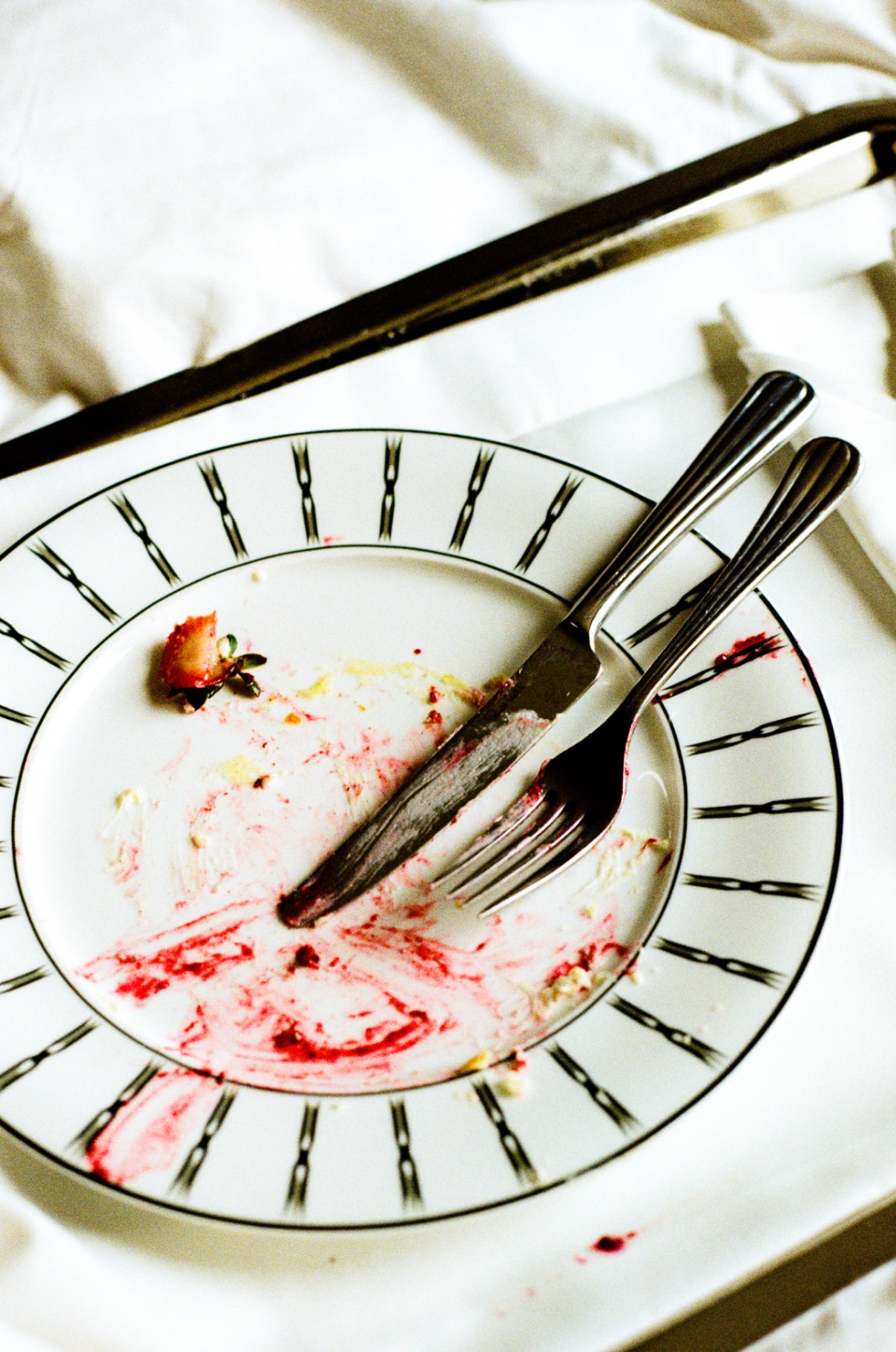 Striped Sommerro plate after breakfast with smeared strawberry and silverware