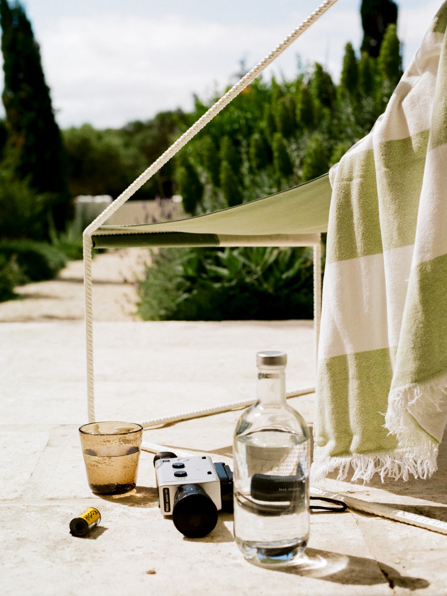 Super 8 camera, amber glass and water bottle under a sail shade