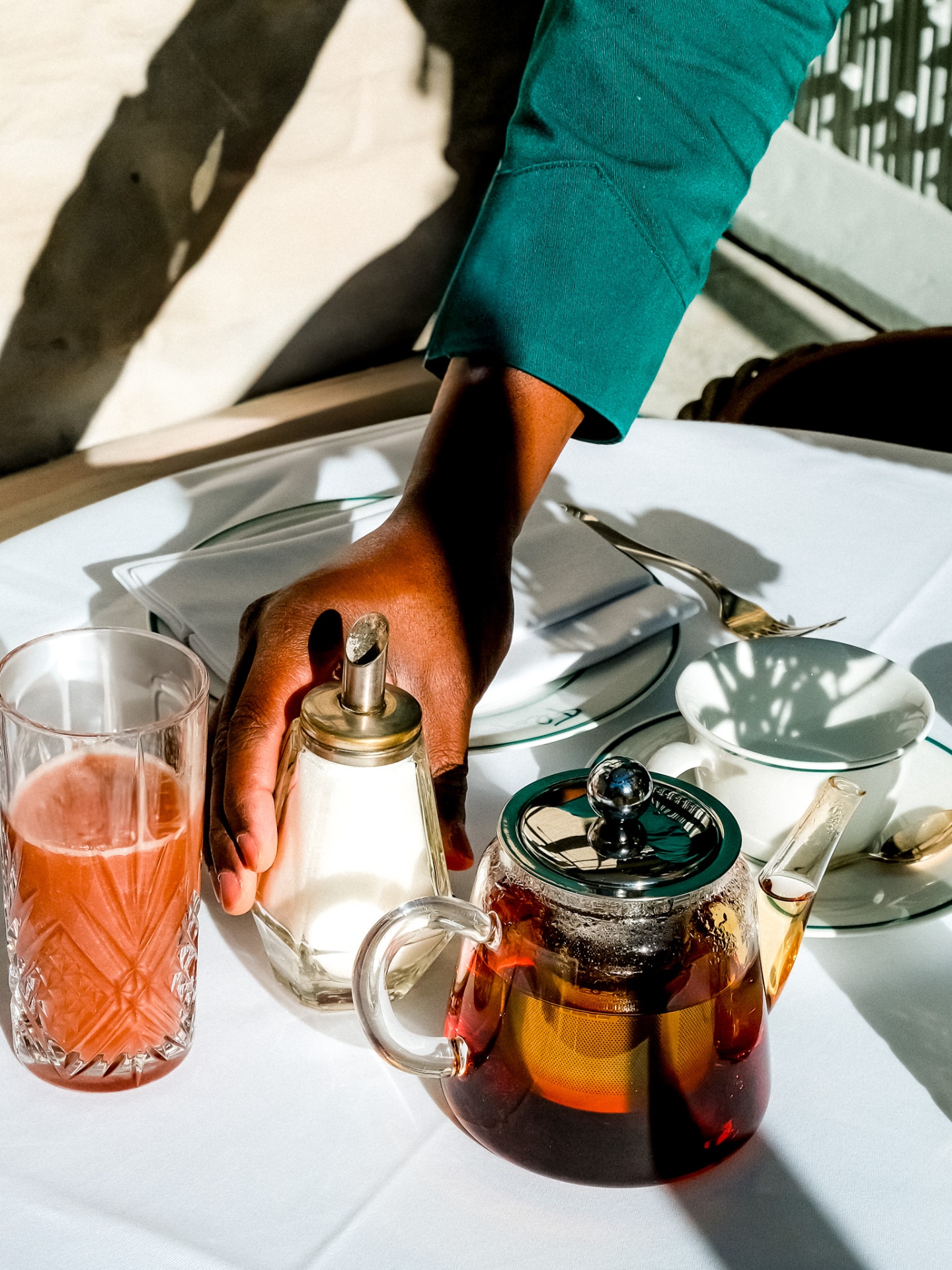 Hand reaching for a sugar shaker beside a glass teapot