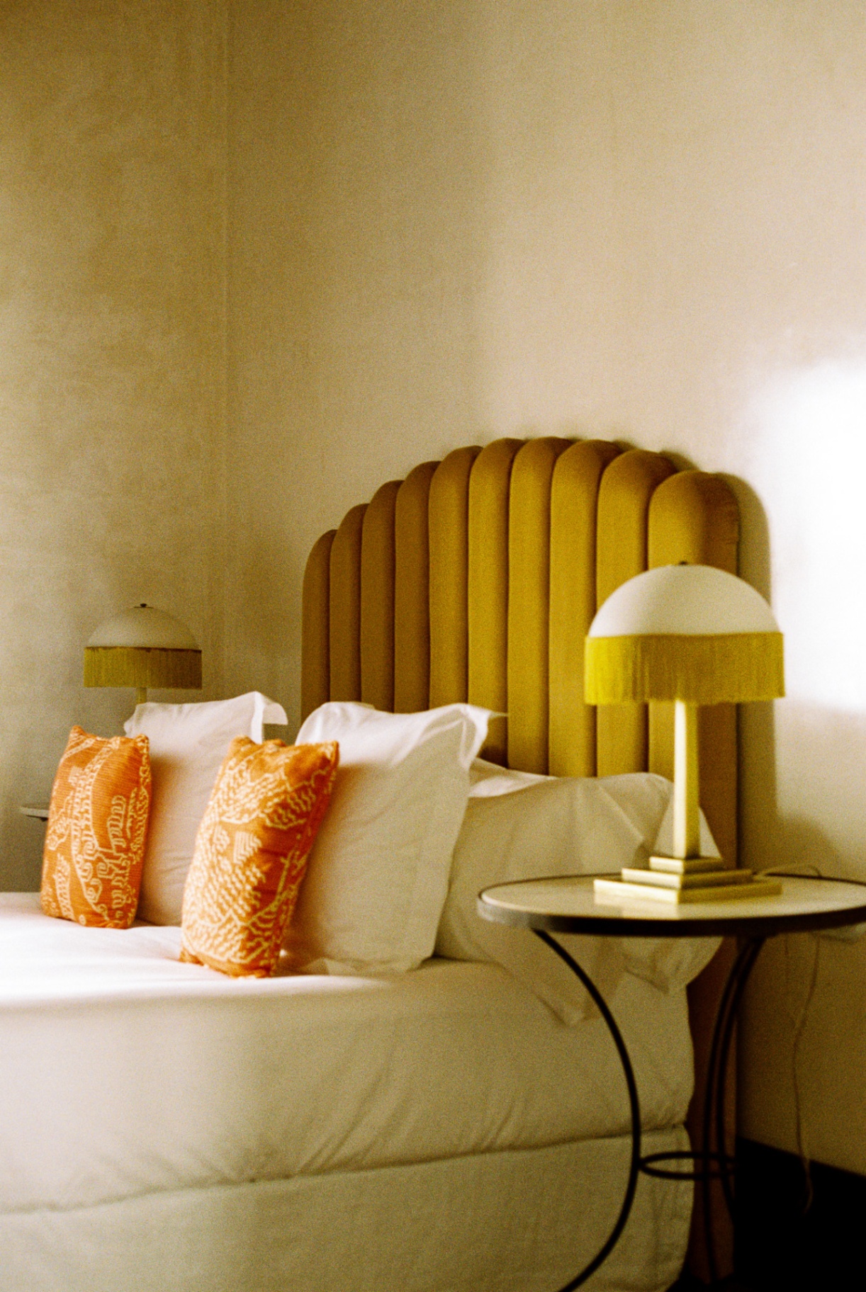 Fluted yellow velvet headboard with fringed lamps and patterned cushions