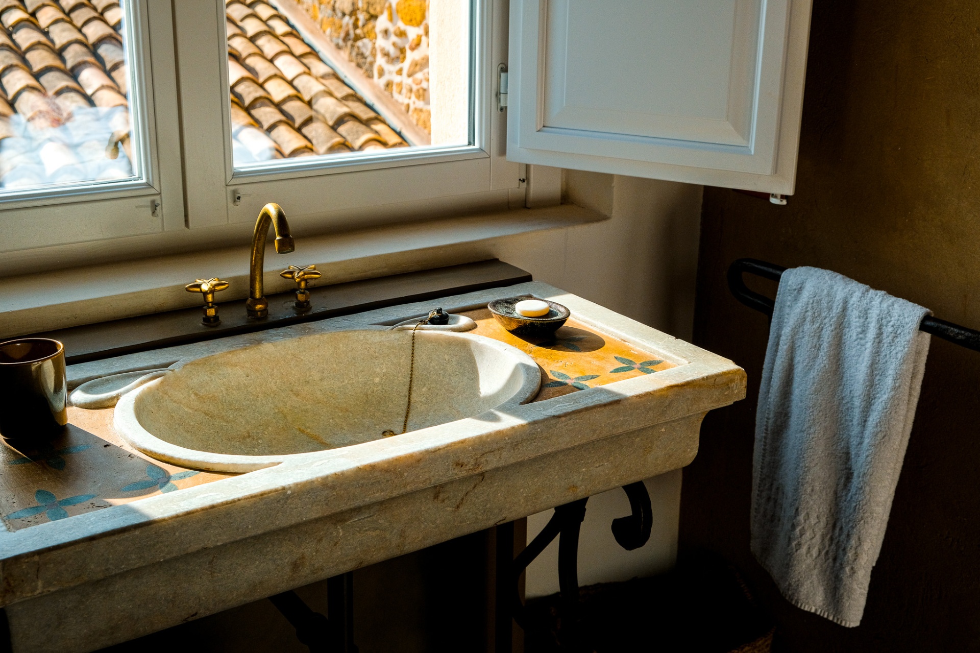 Antique marble sink with brass taps below a shuttered window