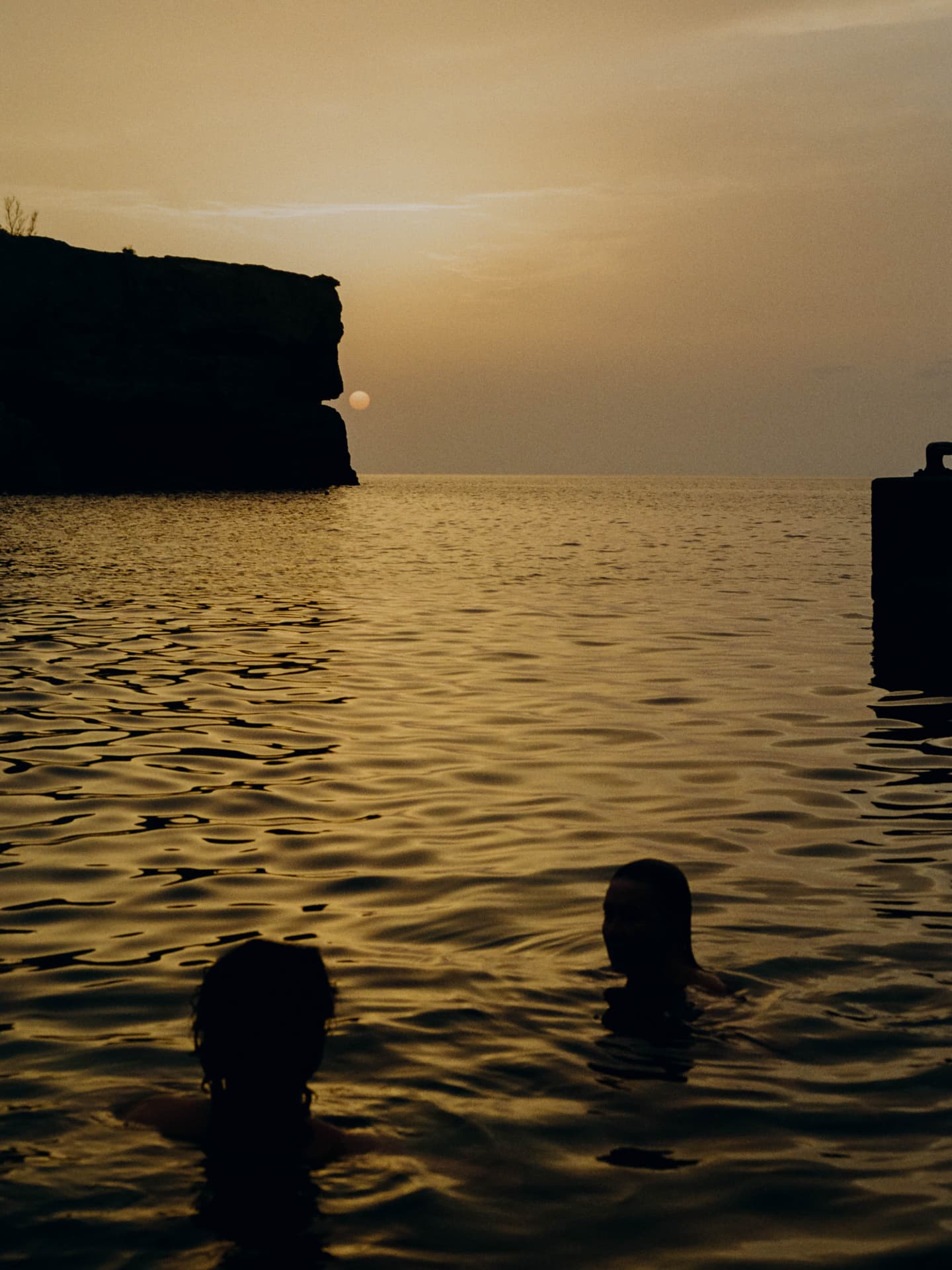 Two swimmers silhouetted in the sea at sunset