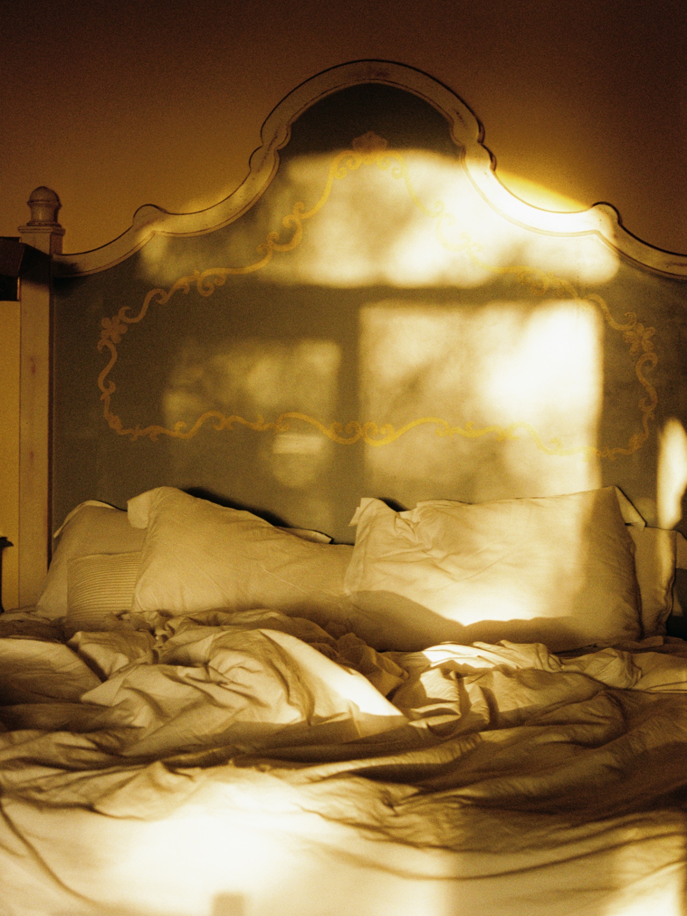 Carved headboard catching late afternoon light over rumpled sheets