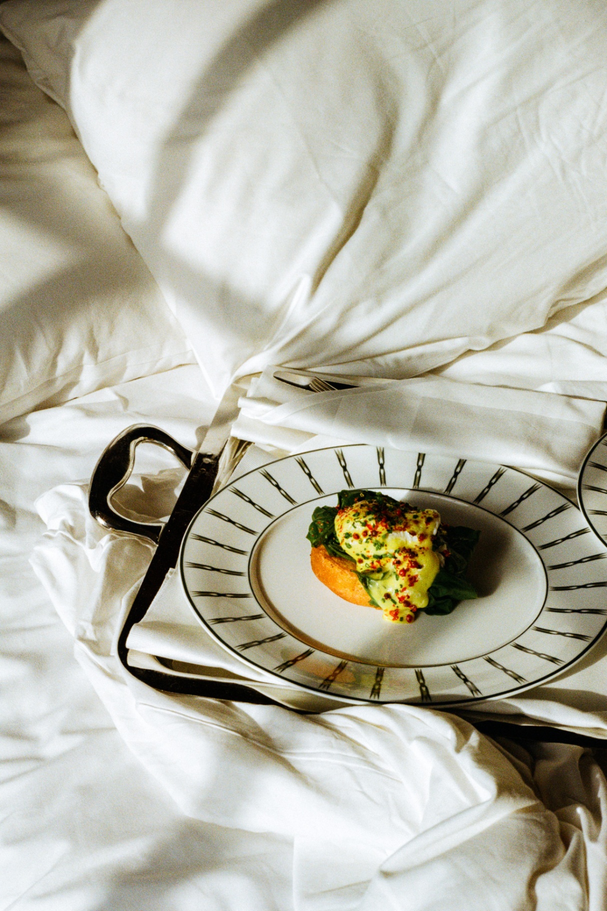 Eggs Benedict served on a striped Sommerro plate atop tousled sheets