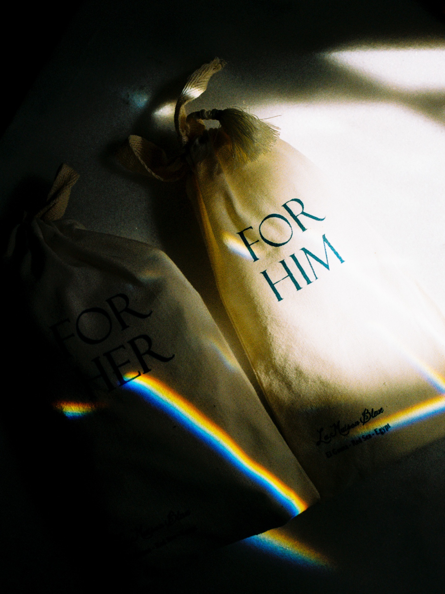'For Him' and 'For Her' linen pouches caught in a prism of light