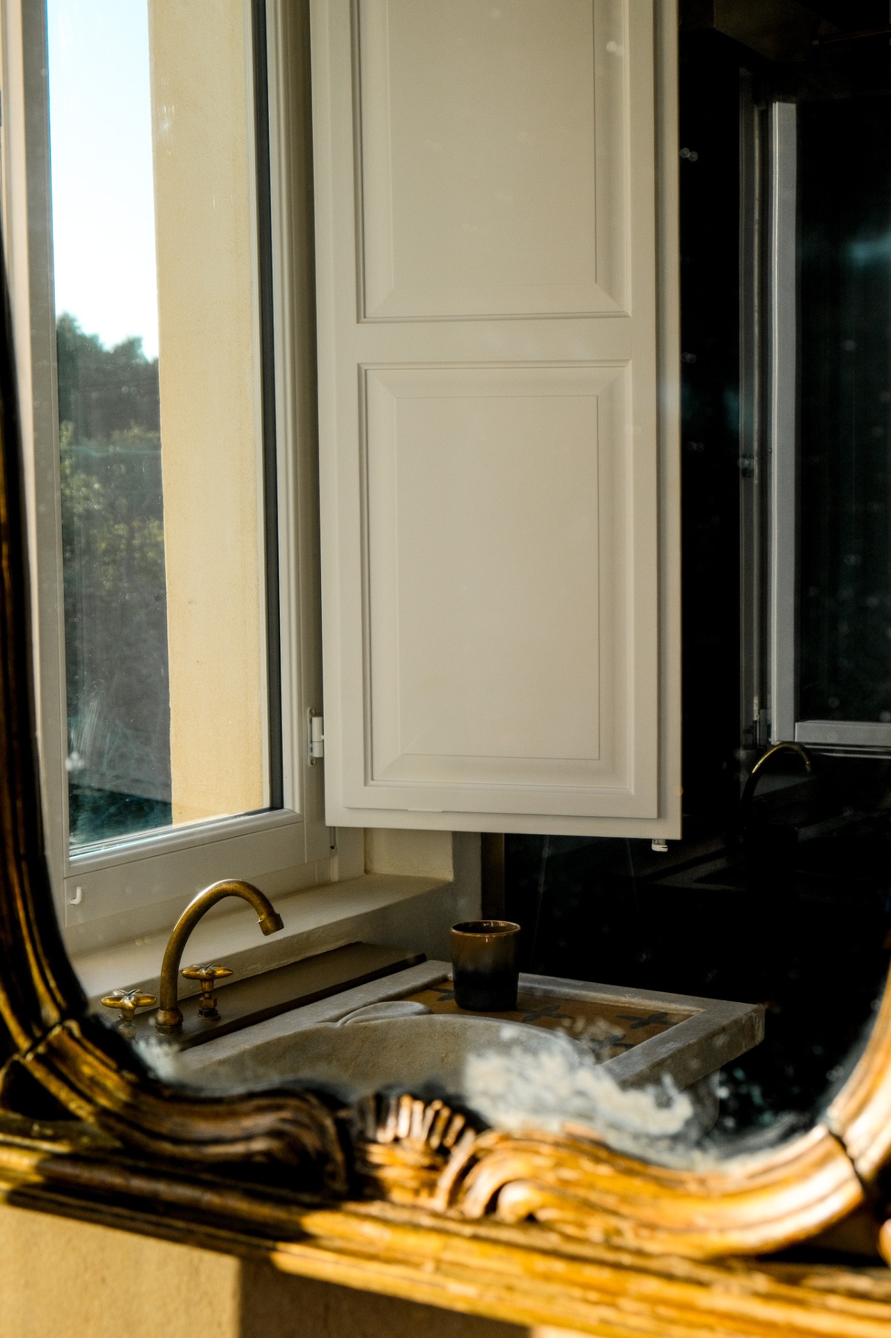 Gilt mirror reflecting an open window above a vintage sink