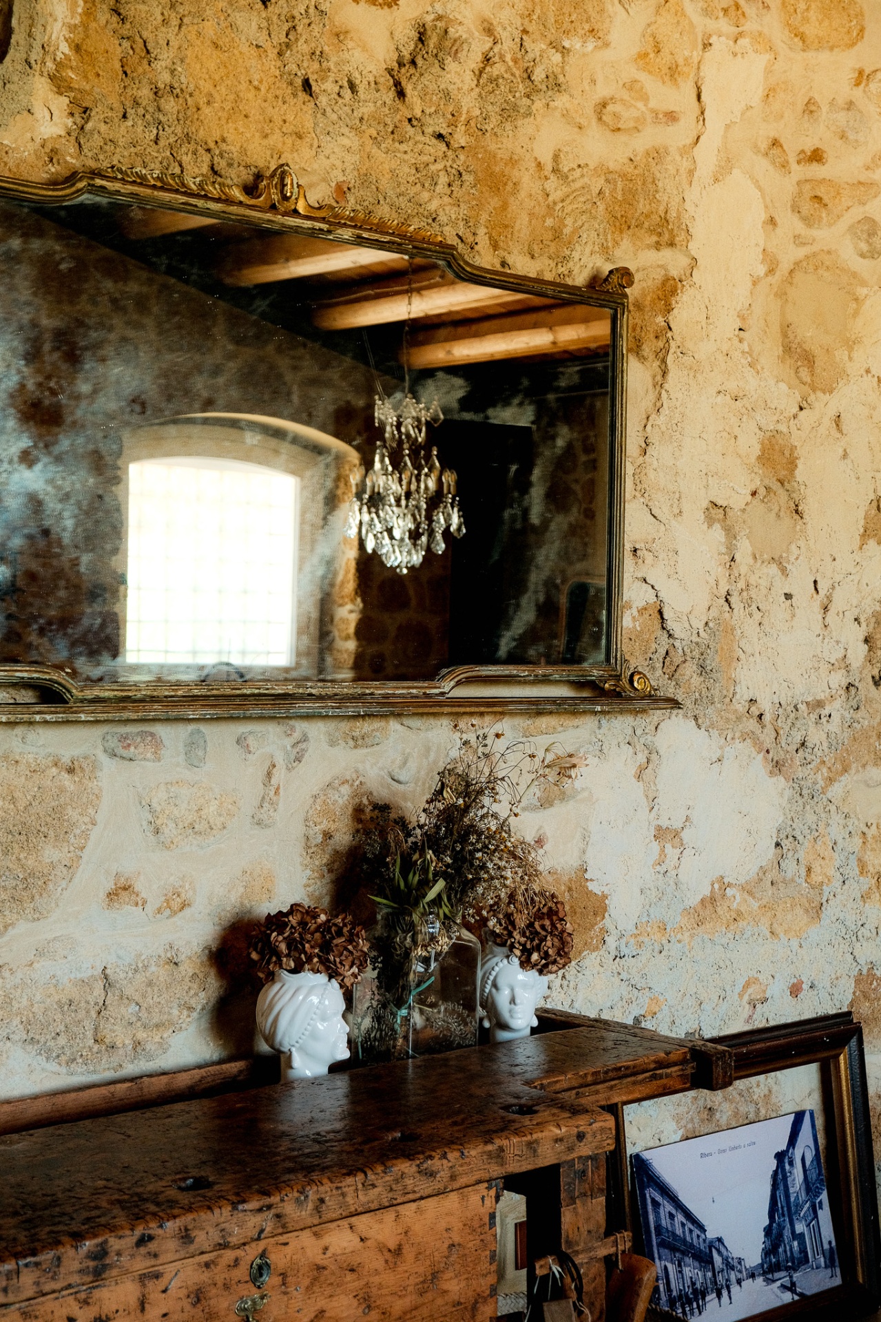 Ornate gilt mirror on a weathered stone wall with dried flowers