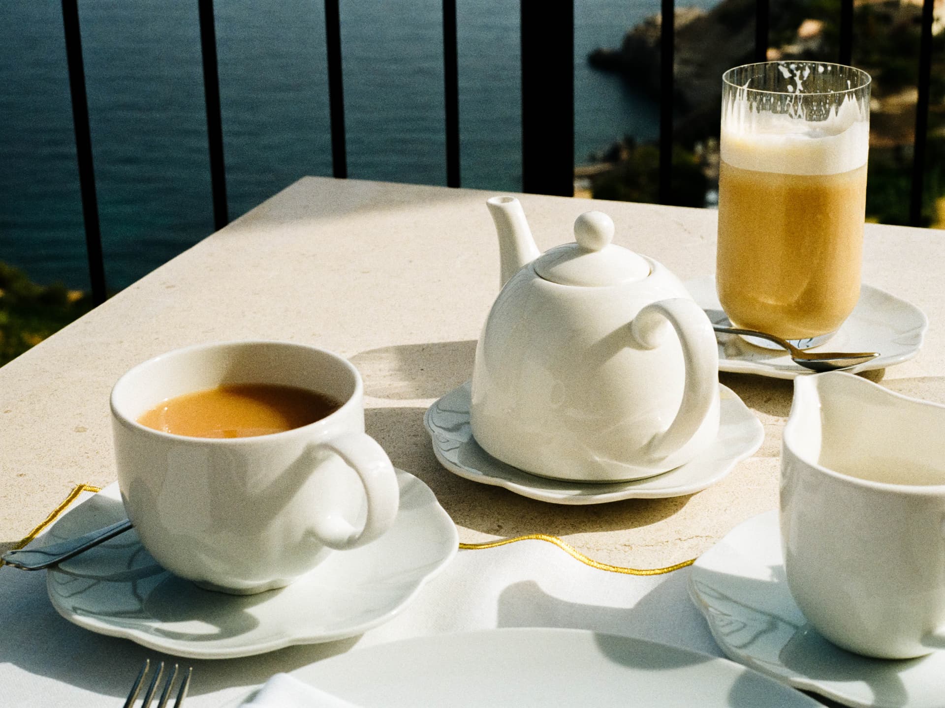 Breakfast tea set on a sunlit terrace table above the sea