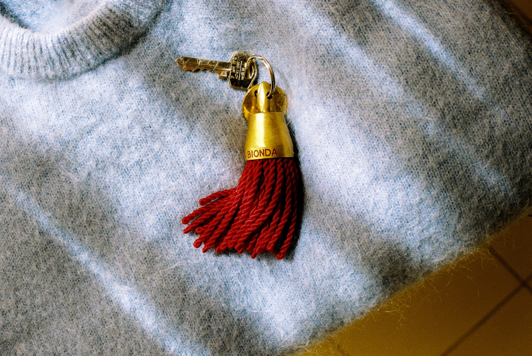 Brass BIONDA keychain with red tassel on a blue knit sweater