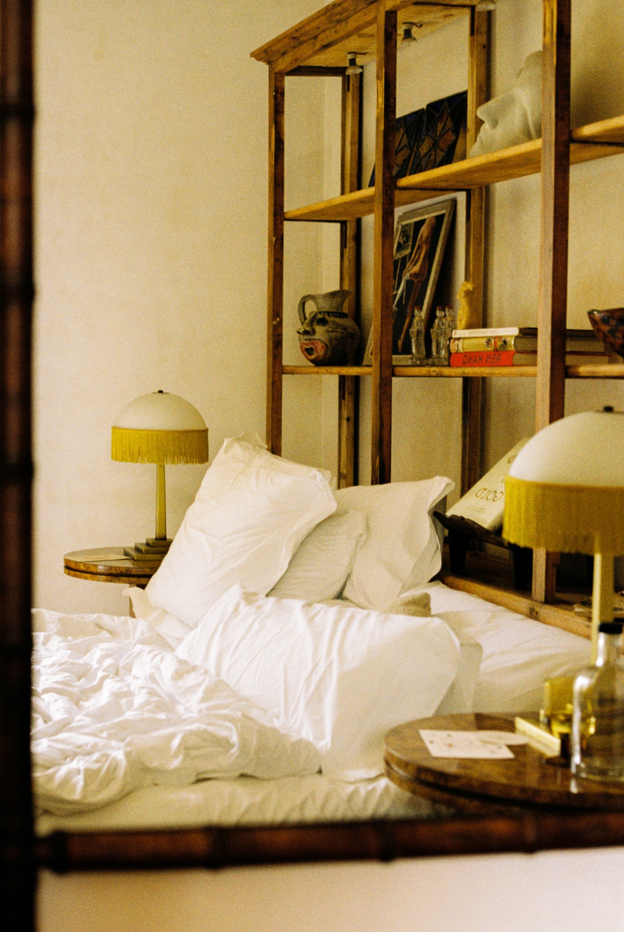 Unmade bed with fringed lamps and a wooden shelving wall behind
